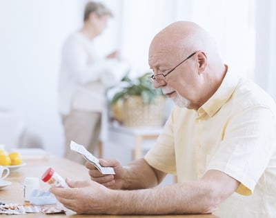 Ein älterer Mann liest sein Medikamentenrezept und hält die Medikamente in der Hand