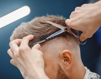 Ein Friseurmeister macht einem Mann mit Geheimratsecken eine Frisur.
