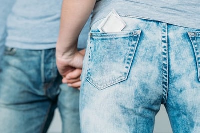  Rückenansicht einer Frau mit einem Kondom in ihrer Jeanstasche als Anspielung auf Safer Sex