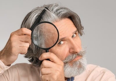 Ein älterer Mann untersucht sein Haar auf Glatzenbildung.