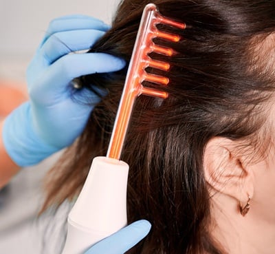 Ein Arzt bürstet das Haar einer Kundin mit einem Lasergerät für Haarwuchs