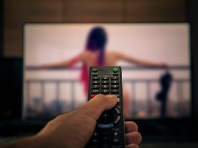  Fernbedienung in der Hand eines Mannes vor dem Hintergrund eines erotischen Films als Konzept von Porno und Masturbation