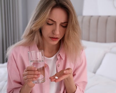 Eine junge Frau mit der Notfallverhütungspille und einem Glas Wasser