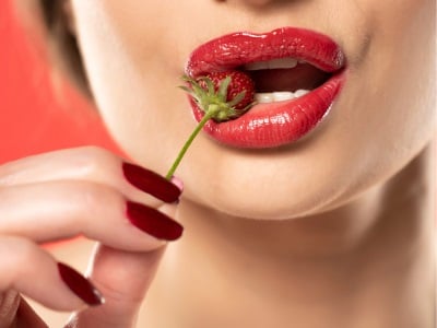Eine Frau mit einer Erdbeere im Mund als Sexualitätskonzept