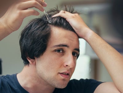 Ein Mann trägt ein Serum auf sein Haar auf, um saisonalen Haarausfall zu verhindern.