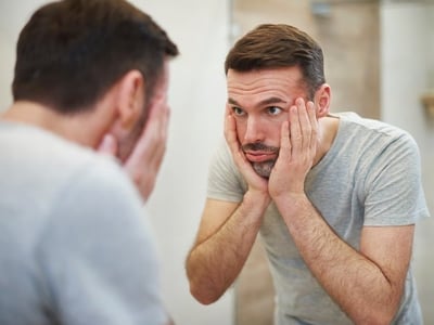 Ein Mann, der traurig in den Spiegel schaut und an Depressionen oder Stress leidet