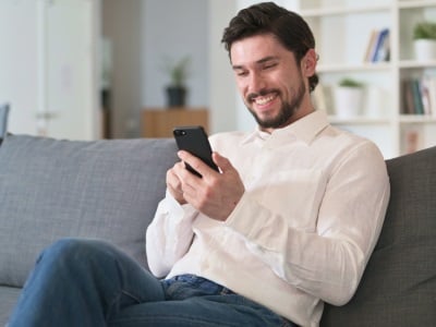 Ein Mann sitzt auf einem Sofa und surft auf seinem Handy.