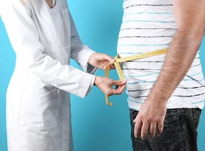 Ein Arzt misst die Taille eines fettleibigen Mannes.
