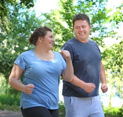 Übergewichtiges Paar läuft fröhlich im grünen Park.