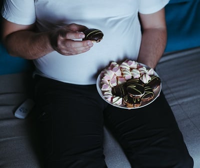  Ein Mann mit Übergewicht, der Süßigkeiten isst und fernsieht.