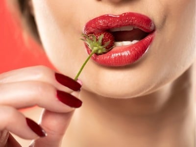 Eine sexy Frau mit einer Erdbeere zwischen ihren roten Lippen