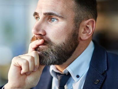 Ein Mann mit Bart und Anzug denkt über etwas nach.