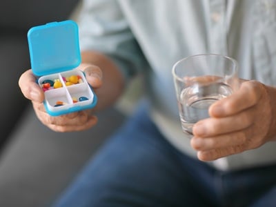 Älterer Mann hält Behälter mit Tabletten und Glas Wasser