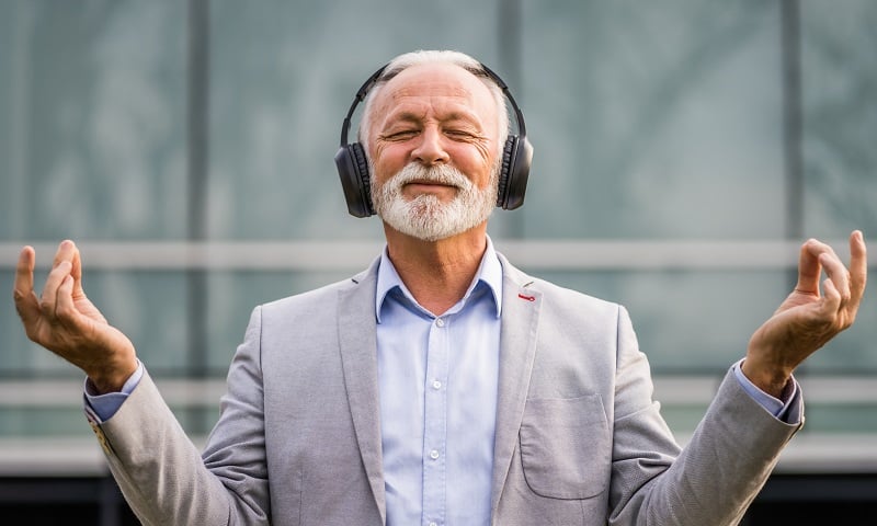 Ein Bild eines älteren Geschäftsmannes, der Musik über Kopfhörer hört und meditiert